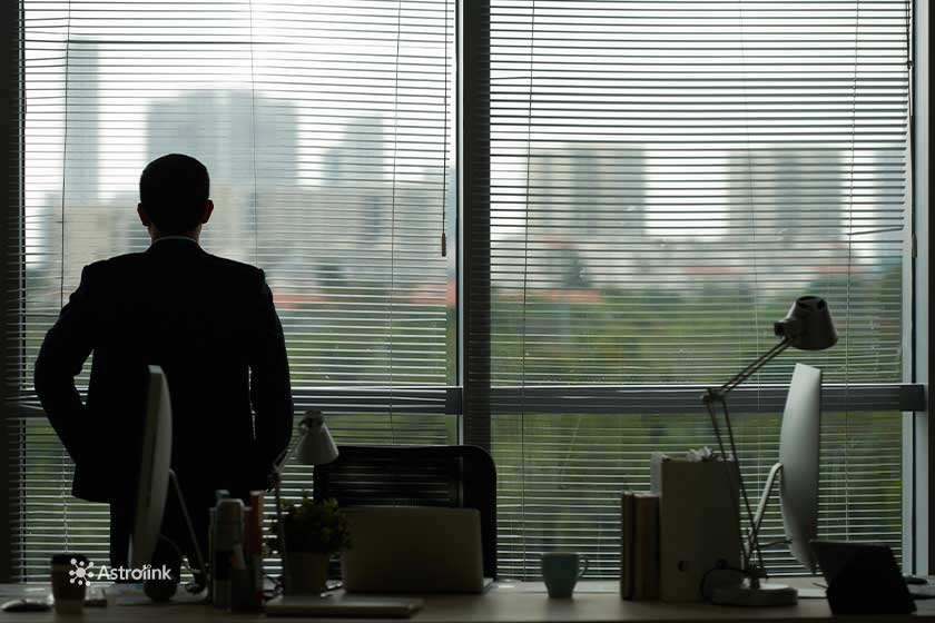 man inside an office, seen from behind, looking at a landscape through the window