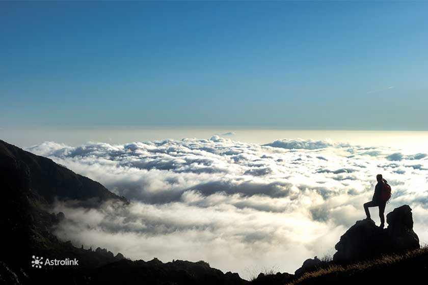 Silhouette of a person standing on a mountain peak, gazing at the clouds